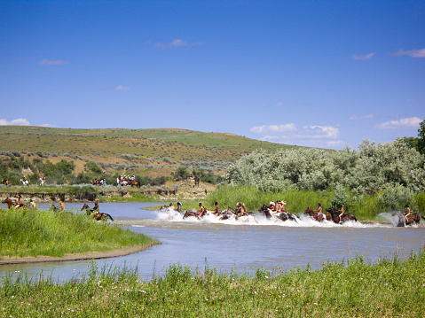 Crow Agency, Montana USA - June 27, 2009: Reenactment of the Battle of the Little Bighorn known as Custer's Last Stand. Young Indian warriors on horseback gallop across the river during battle reenactment.