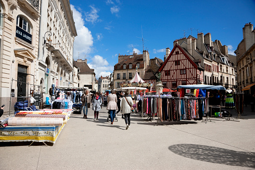 Dijon, France -- April 8, 2016: Market day in Dijon, France. Stalls with merchandise on the the historic city square Place François Rude. People are walking on the square.