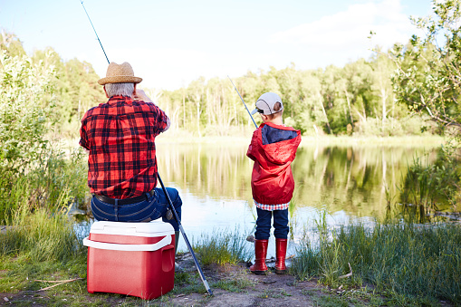 Rear view of grandfather and grandson fishing in pond