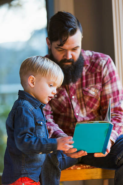 маленький мальчик с отцом, читая книгу - brown hair caucasian little boys men стоковые фото и изображения