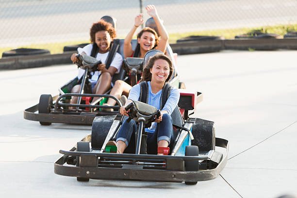 Teenage girls on go carts at an amusement park Multi-ethnic teenage girls riding go carts at an amusement park.  Focus on the girl in front. go carting stock pictures, royalty-free photos & images