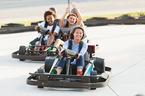 Multi-ethnic teenage girls riding go carts at an amusement park.  Focus on the girl in front.