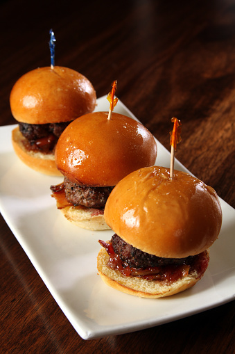 Gourmet hamburger sliders with bacon on white plate with toothpicks