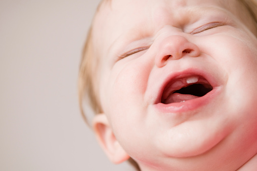Color photo of a crying baby suffering through the teething pain of new teeth coming in.