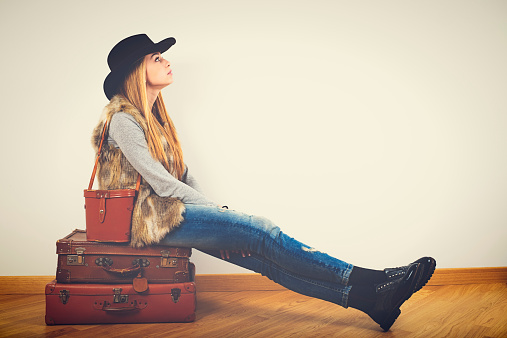 Young woman sitting on vintage suitcases and dreaming about travels, indoors.