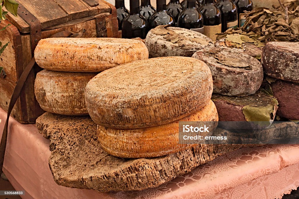 sardinian cheese ripe sheep's milk cheese on a piece of cork and bottles of Italian wine in background - traditional artisan food product  from Sardinia, Italy Sardinia Stock Photo