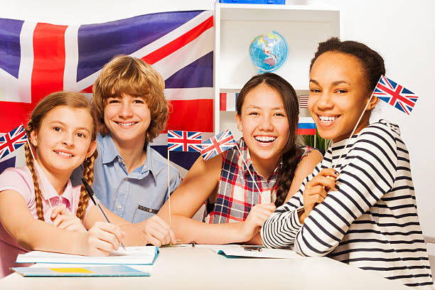 Happy teenage students at language courses Four multiethnic teenage students sitting at the desk, holding British flags at the language courses english culture stock pictures, royalty-free photos & images