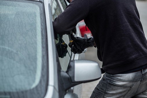 Car thief trying to break into a car with a screwdriver. Car thief, car theft.