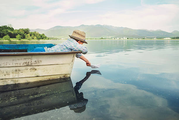 Little boy launch paper ship from old boat on the lake