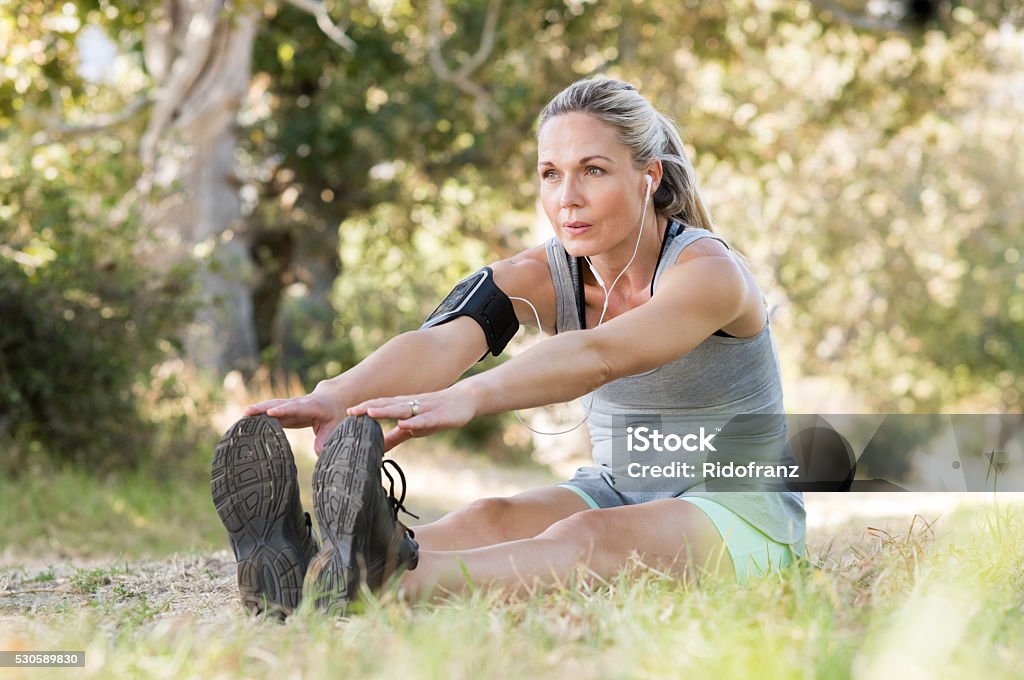 Senior woman stretching Senior woman exercising in park while listening to music. Senior woman doing her stretches outdoor. Athletic mature woman stretching after a good workout session. Mature Women Stock Photo