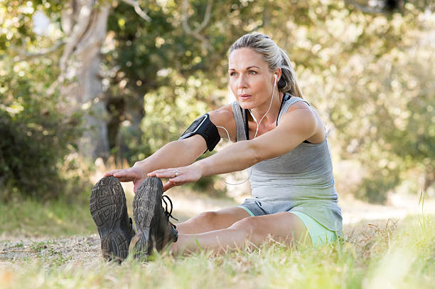 Senior woman stretching Senior woman exercising in park while listening to music. Senior woman doing her stretches outdoor. Athletic mature woman stretching after a good workout session. touching toes stock pictures, royalty-free photos & images