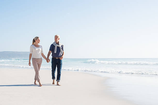 couple marchant sur la plage - holding hands couple senior couple togetherness photos et images de collection