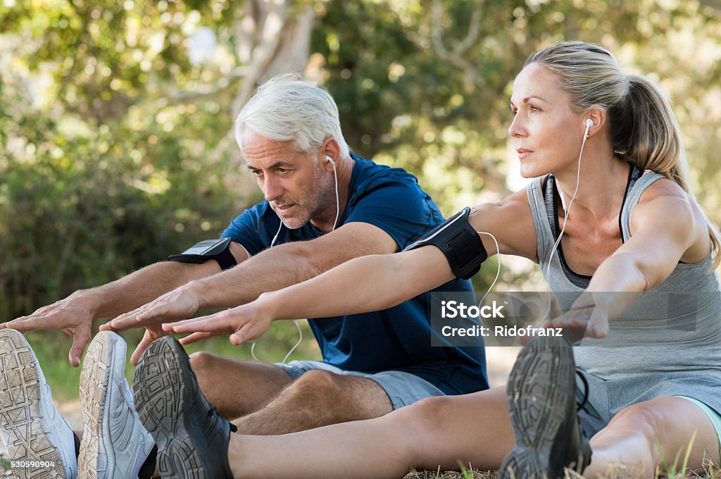 Couple stretching at park Mature couple stretching at park and listening to music. Athletic senior couple exercising together outdoor. Fit senior runners stretching before running outdoors. Exercising Stock Photo