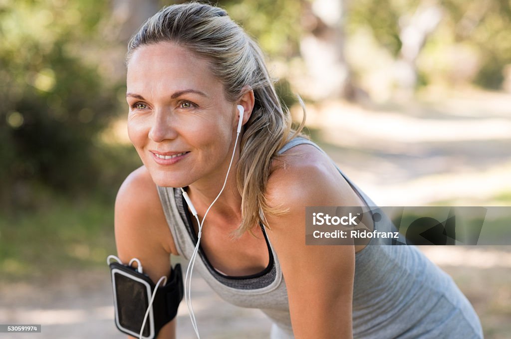 Mature woman jogging Portrait of athletic mature woman resting after jogging. Beautiful senior blonde woman running at the park on a sunny day. Female runner listening to music while jogging. Women Stock Photo