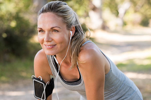 Mature woman jogging Portrait of athletic mature woman resting after jogging. Beautiful senior blonde woman running at the park on a sunny day. Female runner listening to music while jogging. running motion stock pictures, royalty-free photos & images