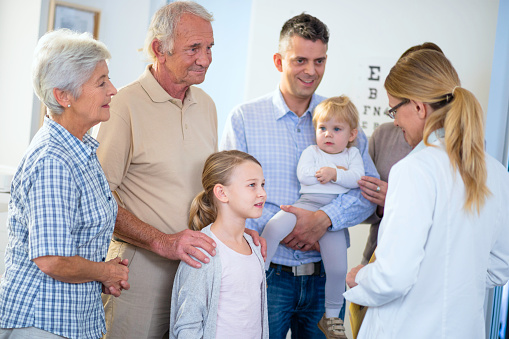 Grandmother and grandfather embracing their young granddaughter and listening to the doctors encouraging words, while the father is holding his youngest daughter and smiling (or possibly flirting) at the female doctor.