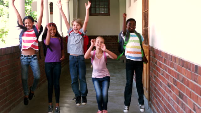 Happy pupils jumping in the air in a hallway in slow motion