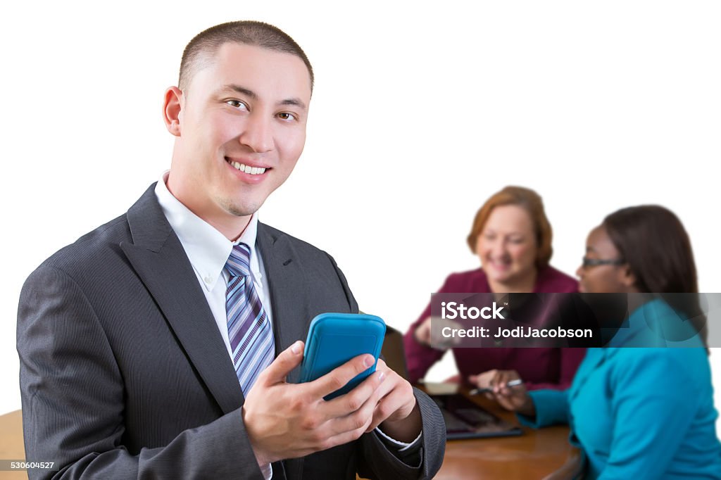 Three business people having a meeting A businessman is having a meeting with two business women. The man is in the front standing with his smartphone in his hands.  The others are seated at a conference table working on a laptop computer.  They are dressed in business attire.  Studio shot isolated on white taken with a Canon 5D Mark 3 camera.  rm Adult Stock Photo