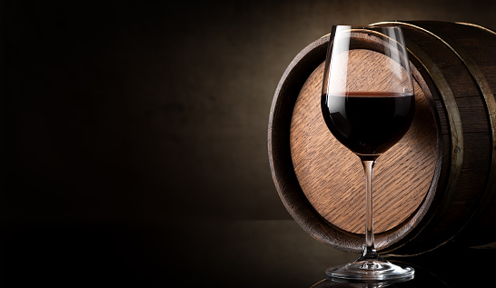Wineglass of red wine and barrel on brown background