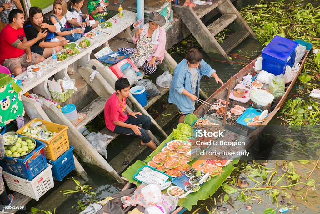 Thai Culture Weekend at Amphawa Floating Market Amphawa, Thailand - December 6, 2014: On a holiday weekend Thai people spend time eating along a traditional floating market. Food is prepared and cooked on a wooden long tail boat in the river. Floating Market Stock Photo