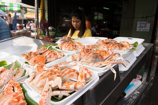 Amphawa, Thailand - December 6, 2014:A woman works behind a seafood stand along the traditional floating market. Whole fresh crabs are set out for sale.