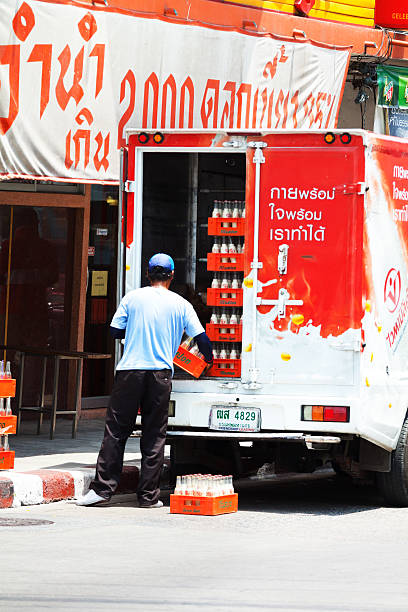 Bangkok, Thailand - April 25, 2014: Capture of a Thai man delivering milk in Bangkok. Man is standing in back of cooled truck and is carrying boxes with milk bottles. Inside of truck are many bottles. Car is red colored with waves of milk. In background is a store. Scene is in street Chokchai 4, Ladprao.