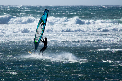 Tenerife, Spain-november 29, 2014: Windsurfer with blue sail among the waves in a windy and sunny autumn day in front of \