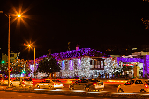 Bogota, Colombia - December 25, 2014: The older section the Hacienda Santa Barbara shopping mall, right on Carrera Septima, in Bogota, the capital city of Colombia in South America, has been lit up with decorative LED lights to celebrate Christmas. Traffic whizzes by on the carrera. The illumination draws crowds both local and tourists. Shadows and silhouettes of people can be seen in from of the mall. Photo shot in the horizontal format; a long exposure of 6.0 seconds creates some motion blur and light trails.  Copy space.