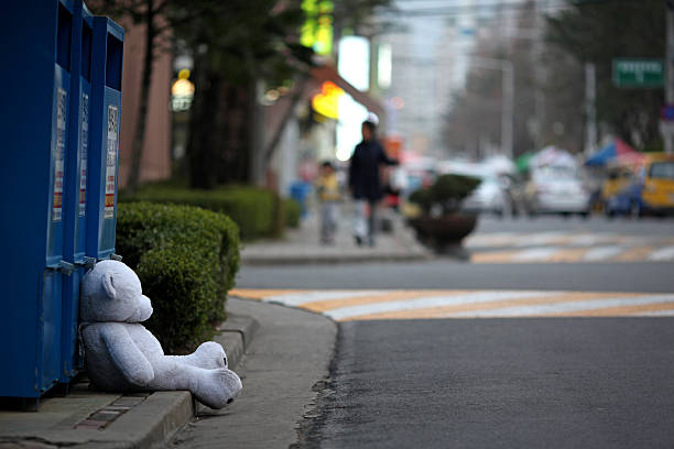 Changwon, South Korea - March 19, 2013: A white teddy bear sits on the sidewalk next to some clothing donation bins.