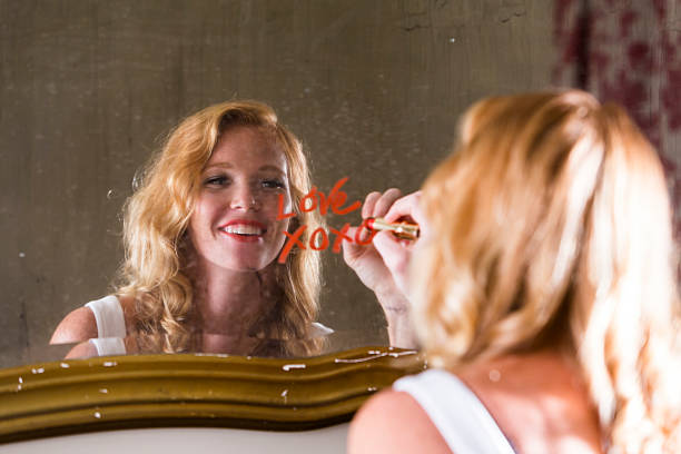 Romantic young woman in love Beautiful, smiling young woman writing the word LOVE and XOXO with red lipstick on a mirror. Focus on the woman's reflection. mirror writing stock pictures, royalty-free photos & images