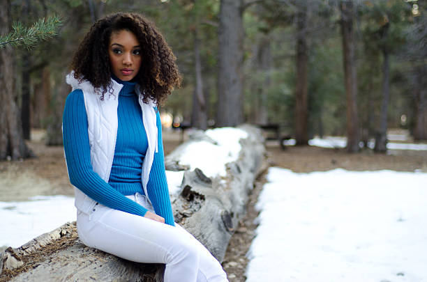 Teenaged mixed race female with curly hair wearing winter attire sitting on a tree.Natural light on location in Southern California mountains.