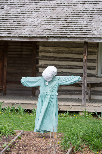 An old scarecrow is on display in front of a wooden plantation home.  