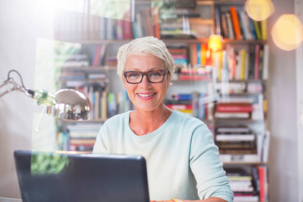 Businesswoman smiling at computer in home office  baby boomer stock pictures, royalty-free photos & images