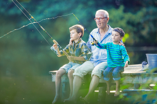Cute Redhead Boy and Grandparents Fishing in the River in Quebec. The grandfather and the grandmother are teaching their grandson how to fish.