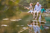 istock Grandfather and grandsons fishing and playing with toy sailboat at lake 530682409