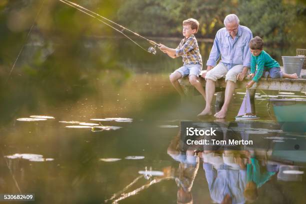 Grandfather And Grandsons Fishing And Playing With Toy Sailboat At Lake Stock Photo - Download Image Now