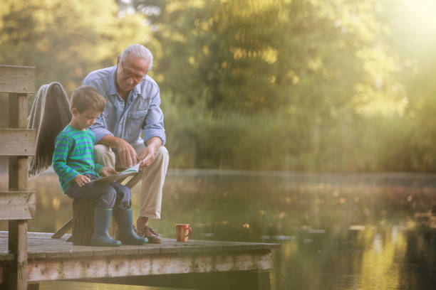 nonno e nipote che leggono al lago - men reading outdoors book foto e immagini stock