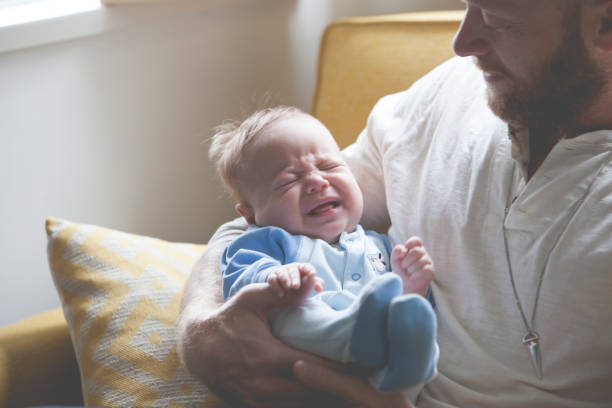 istock Father holding and looking at crying baby, sitting on sofa 530682533