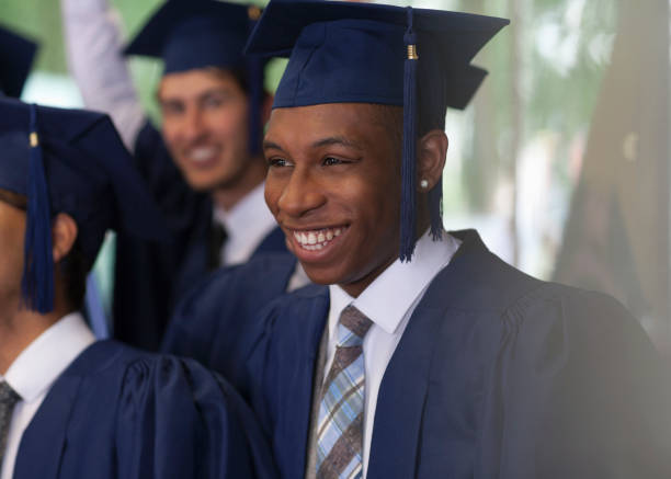 улыбающиеся студенты университета, стоящие на открытом воздухе во время выпускной церемонии - graduation university male student стоковые фото и изображения