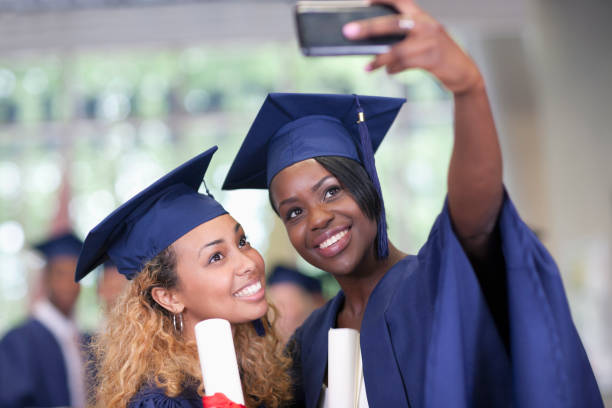 Four cheerful multi-ethnic students wearing graduation gowns and caps gesturing peace sign