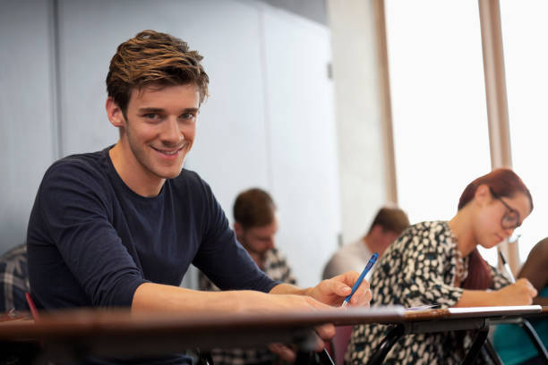 istock Male student smiling at camera and sitting at desk during lecture 530683187