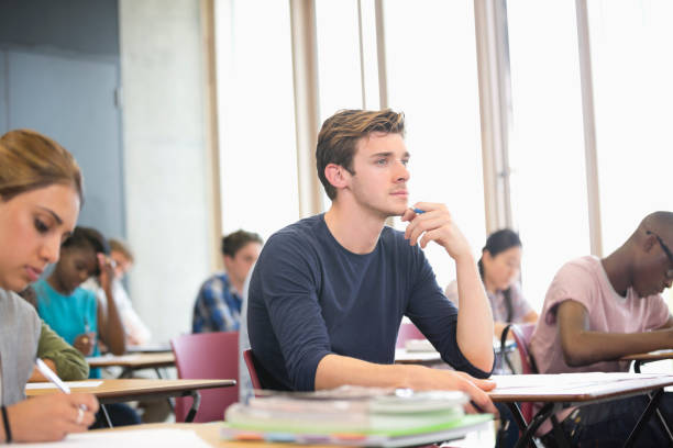istock Male student with hand on chin during lecture with other students in background 530683195