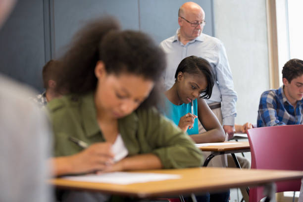 istock Teacher walking along desks and checking students during test 530683205