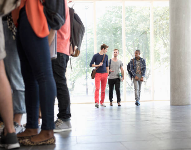 istock Three male students walking along corridor talking with large window in background 530683207