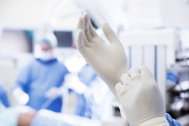 primer plano del cirujano poniéndose guantes quirúrgicos en quirófano - surgical glove fotografías e imágenes de stock