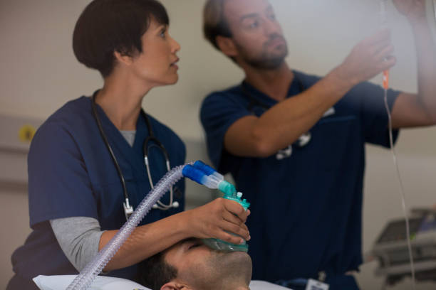 患者の上に酸素マスクを保持している医師、集中治療室で点滴を調節する医師 - 18813 ストックフォトと画像