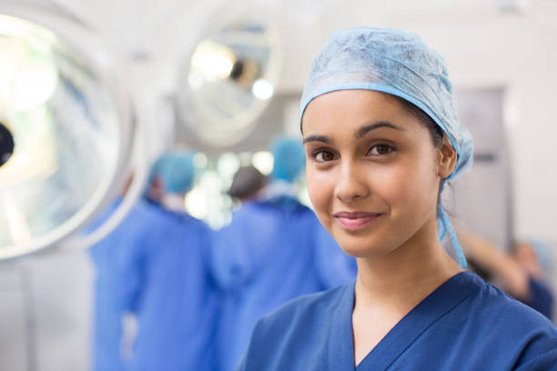 portrait of smiling female surgical nurse wearing blue surgical cap and scrubs - female nurse imagens e fotografias de stock