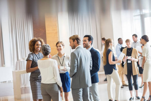 group of business people standing in hall, smiling and talking together - business people stok fotoğraflar ve resimler