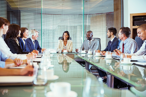 Happy businesspeople smiling cheerfully in a meeting room. Group of successful businesspeople sitting together during their morning briefing in a modern office. Colleagues working together.