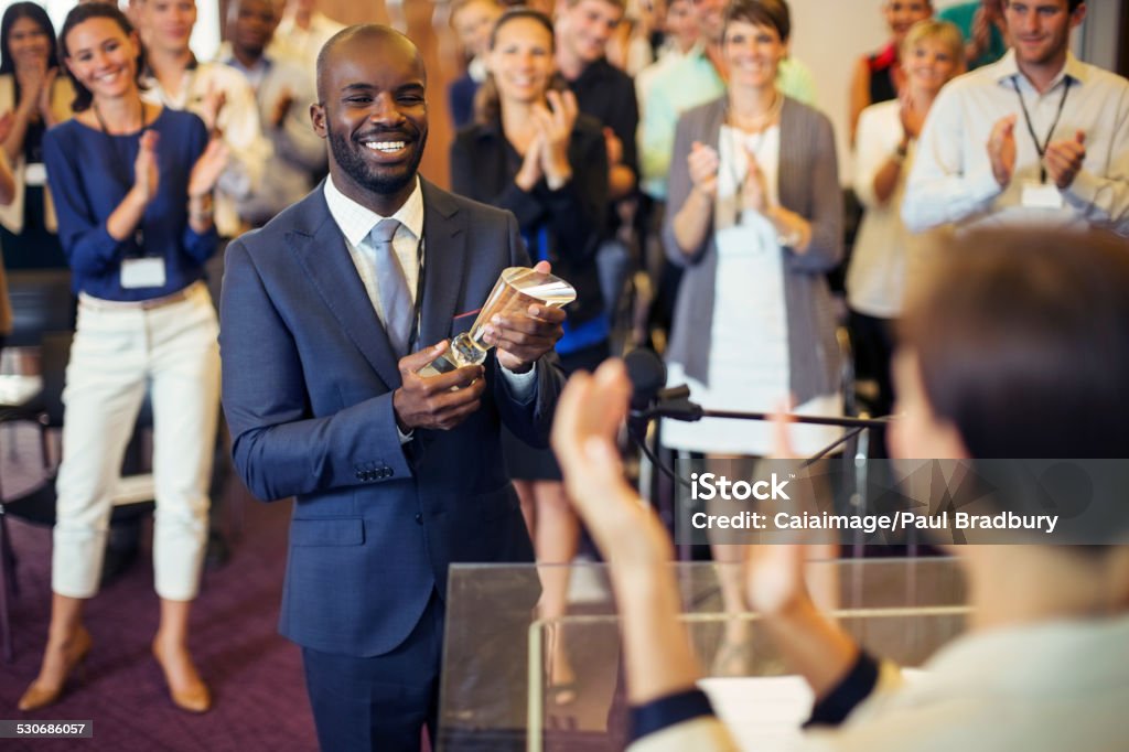 Portrait of young man holding trophy, standing in conference room, smiling to applauding audience  Awards Ceremony Stock Photo